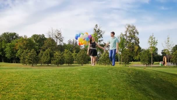 Vídeo en cámara lenta de feliz pareja joven caminando en el parque con un montón de globos de colores — Vídeos de Stock