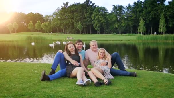 Vídeo em câmera lenta de dois casais relaxando junto ao rio no parque — Vídeo de Stock