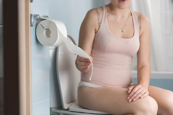 Imagem de close-up da jovem mulher sentada no banheiro e puxando papel higiênico — Fotografia de Stock