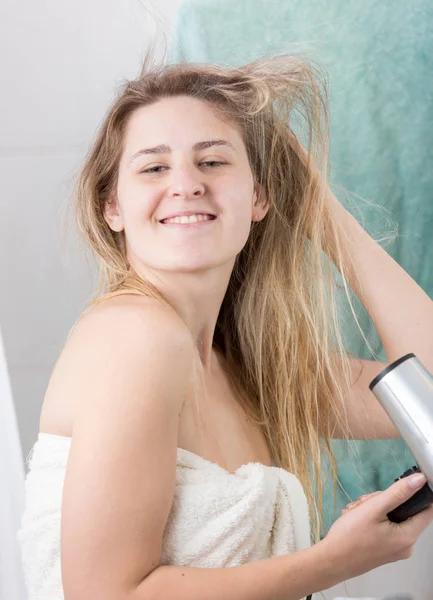微笑的愉快的妇女干燥长的头发的画像用吹风机 — 图库照片