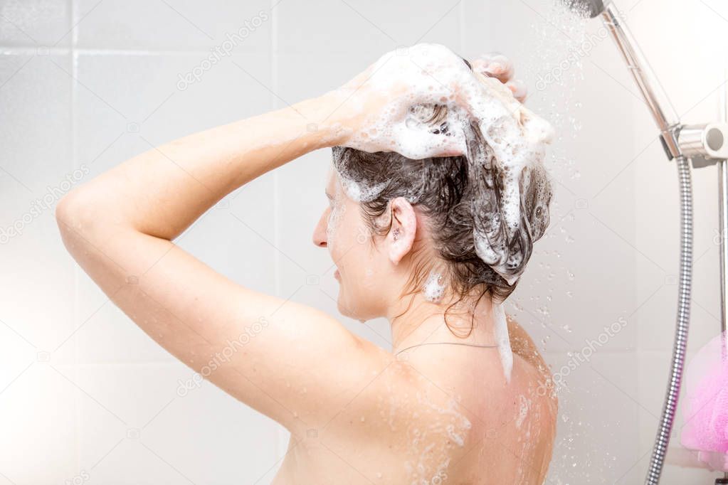 Rear view image of young brunette woman washing hair with shampoo