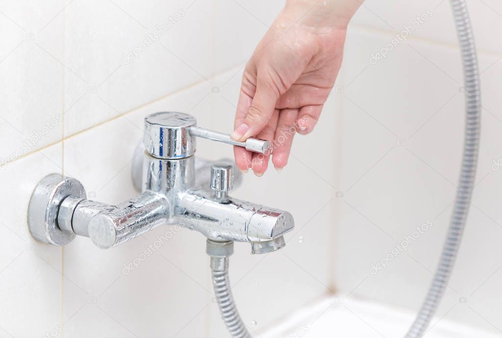 Closeup image of young owman pulling metal handle on water tap in shower