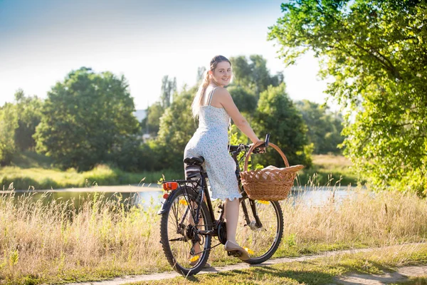 Bela jovem sorrindo mulher no verão vestido psoing com bicicleta no campo — Fotografia de Stock