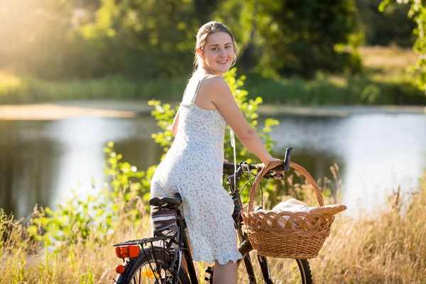 Retrato de uma jovem mulher sorrindo andando de bicicleta no campo e olhando sobre o ombro na câmera — Fotografia de Stock