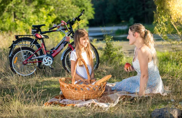 Beautiful young woman having picnic with girl at river — Stock Photo, Image
