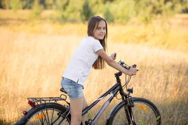 Belle adolescente avec des cheveux longs équitation vélo dans le champ — Photo