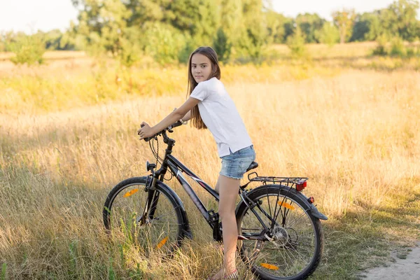 Beautiful brunette girl riding mountain bike in field at sunset — Stock Photo, Image