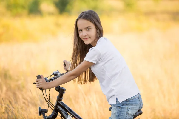 Portrait of beautiful brunette girl sitting on bicycle at field — Stock Photo, Image