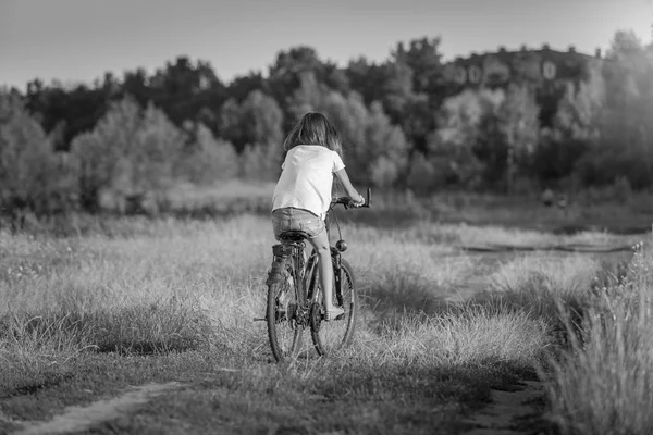 Black and white image of young girl in shorts riding bibcycle on path at field — Stock Photo, Image