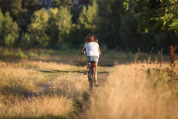 Zadní pohled obraz mladé dospívající dívky jedoucí na kole na cestu v poli — Stock fotografie