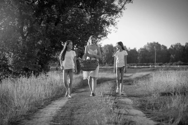 Zwart-wit afbeelding van twee meisjes lopen met moeder naar picknick in veld — Stockfoto