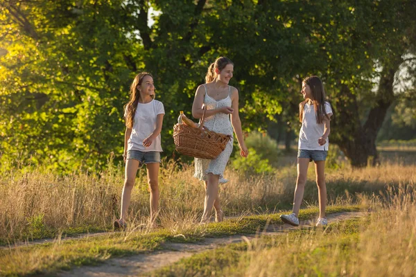 Duas meninas adolescentes andando com a mãe no campo ao pôr do sol — Fotografia de Stock