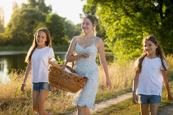 Retrato de una hermosa joven caminando con dos hijas cerca del lago al atardecer — Foto de Stock