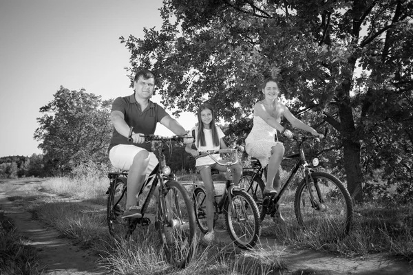 Black and white image of happy parents riding bicycles with daughter in park — Stock Photo, Image