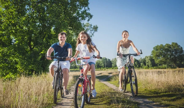 Imagen tonificada de linda niña de 10 años montando bicicletas con los padres en el campo — Foto de Stock