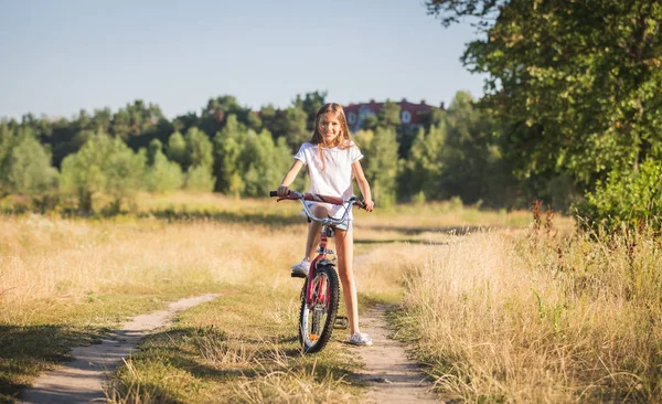 Stonowanych obraz piękny uśmiechający się teenage girl pozowanie na rowerze w dziedzinie — Zdjęcie stockowe