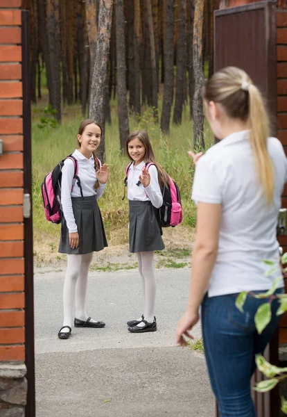 Due ragazze carine in partenza per la scuola a mnorning e agitando alla madre — Foto Stock