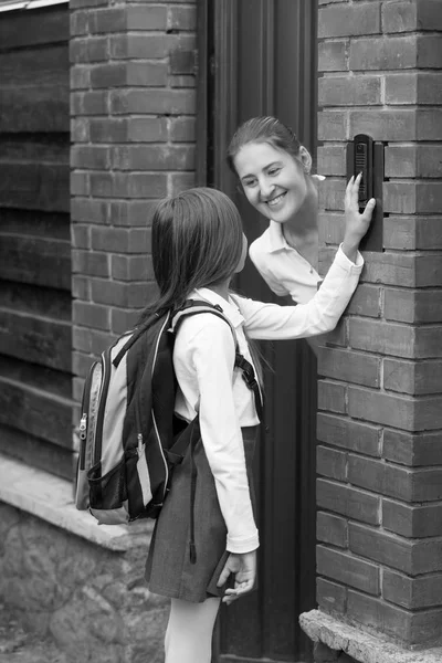 Zwart-wit beeld van de jonge moeder opent de deur naar haar dochter na het gaan naar school — Stockfoto