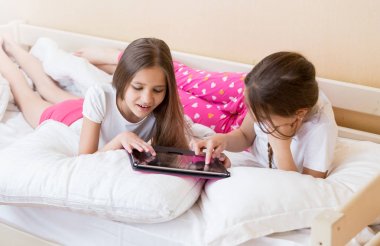 İki genç kız yatakta yatarken ve dijital tablet kullanarak pijama