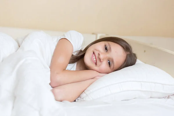 Closeup portrait of beautiful smiling girl lying on pillow at bed — Stock Photo, Image
