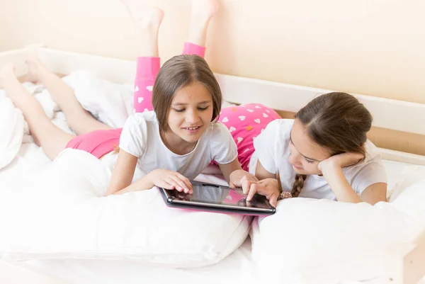 Duas meninas deitadas na cama e assistindo vídeo no computador tablet — Fotografia de Stock