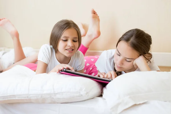 Closeup portrait of two teenage sisters using tablet computer on bed — Stock Photo, Image