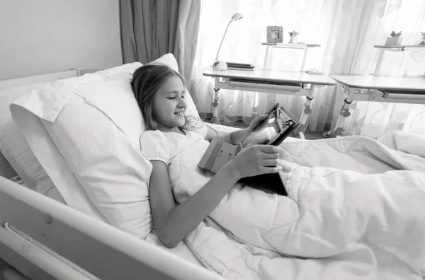 Genç kız yatakta yatan ve dijital tablet bilgisayar kullanarak siyah beyaz portre — Stok fotoğraf