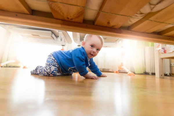 Blick unter das Bett des niedlichen lächelnden Kleinkindes, das im Schlafzimmer krabbelt — Stockfoto