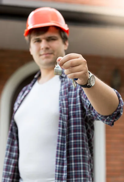 Portret van de jonge mens in veiligheidshelm houdt sleutels uit nieuw huis — Stockfoto