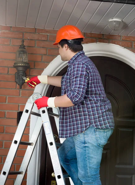 Mannelijke reparateur permanent op trapladder en herstellen van buiten lamp — Stockfoto