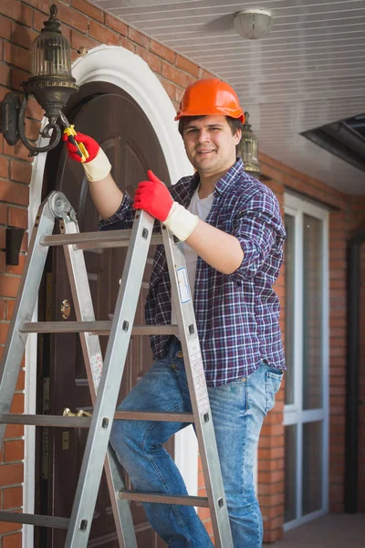 Portrait of smiling young electrician repeiring street light in house — Stock Photo, Image