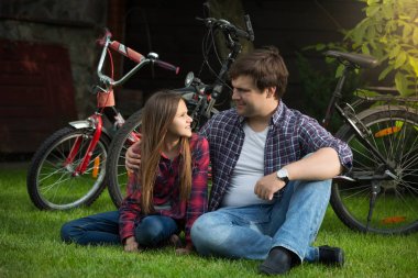 Gülümseyen kız bisiklet sürme sonra Park çimenlerin üzerinde oturan babası bakarak