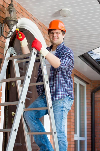 Portret van lachende klusjesman klimmen op trapladder te repareren lantaarnpalen — Stockfoto