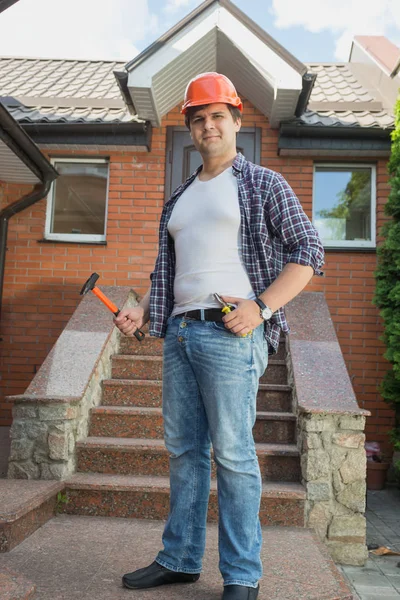 Молодий чоловік у картатій сорочці позує з інструментами перед входом до дому — стокове фото