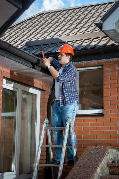 Jonge mannelijke bouwer permanent op trapladder en op het dak repareren — Stockfoto