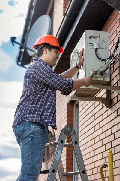 Mannelijke reparateur permanent bovenop trapladder en tot vaststelling van de airconditioner — Stockfoto