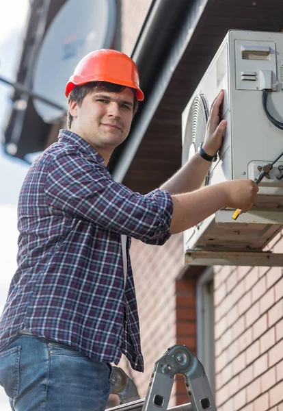 Porträt eines jungen Elektrikers, der Außeneinheit einer Klimaanlage repariert — Stockfoto