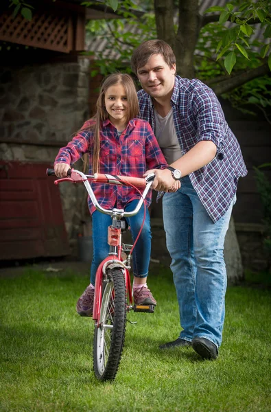 Portrait of smiling young man pushing his daughter learning how to ride bicycle — Stock Photo, Image