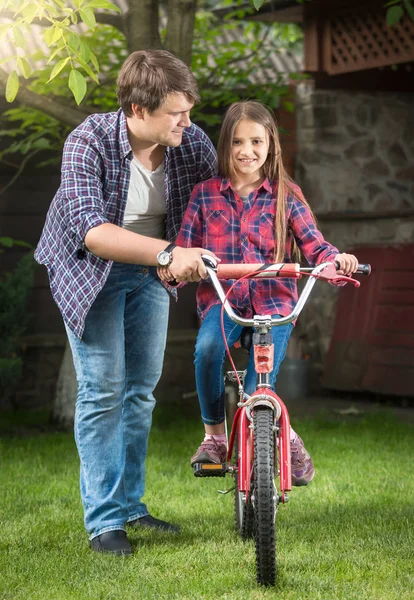 Молодой красивый мужчина учит свою дочь кататься на взрослых велосипедах в парке — стоковое фото