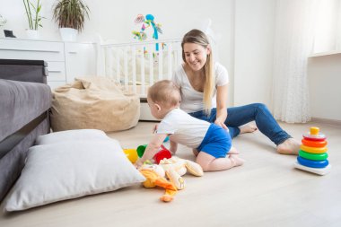 Mutlu genç kadın yatak odası katında onun yürümeye başlayan çocuk ile oynamak