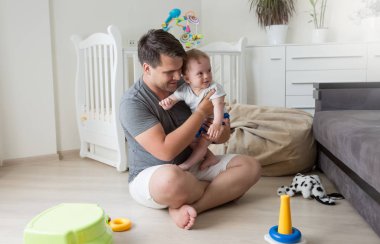 Mutlu genç Baba katta oturan ve onun erkek bebek sarılma