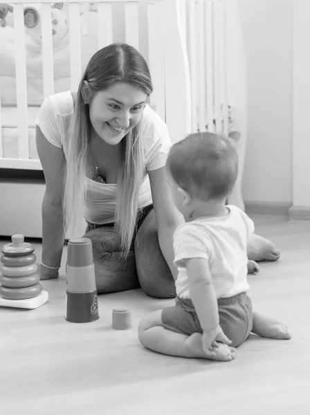 Foto en blanco y negro de la hermosa madre joven sentada en el suelo y sonriendo a su hijo pequeño — Foto de Stock