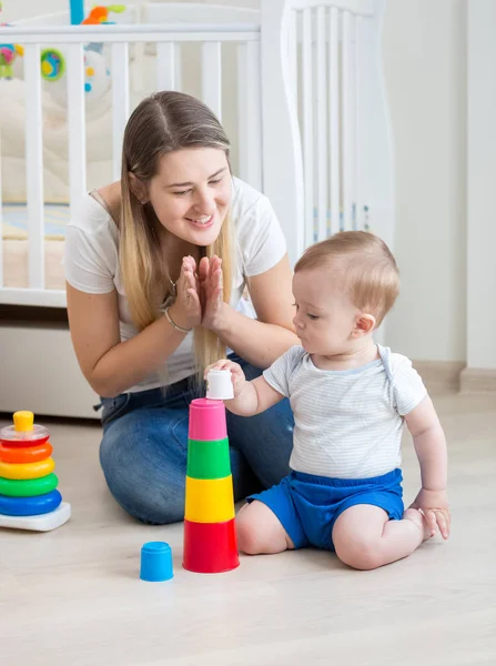 快乐的年轻母亲欢呼, 而她的蹒跚学步的男孩从玩具积木大厦塔 — 图库照片