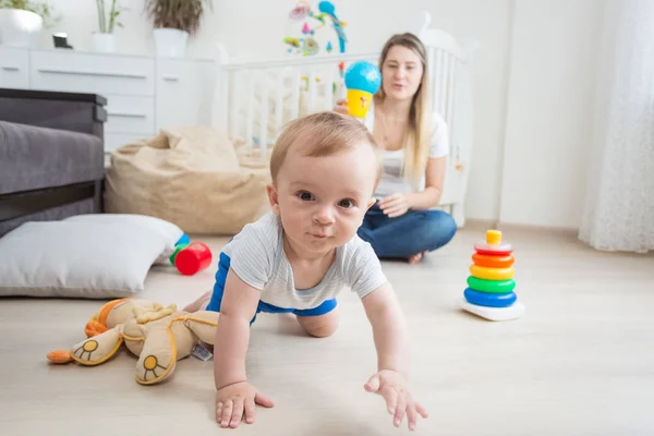 Porträtt av söt 10 månader gammal pojke leker på golvet med mamma och tittar på kameran — Stockfoto