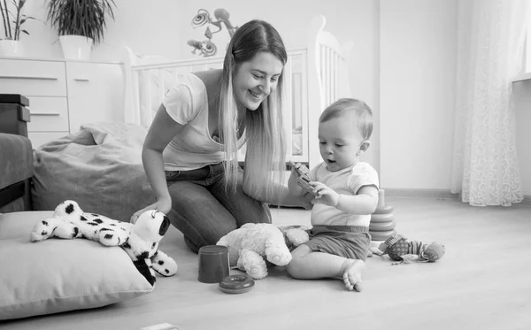 彼の母が付いている床で遊ぶ愛らしい幼児男の子の黒と白の写真 — ストック写真