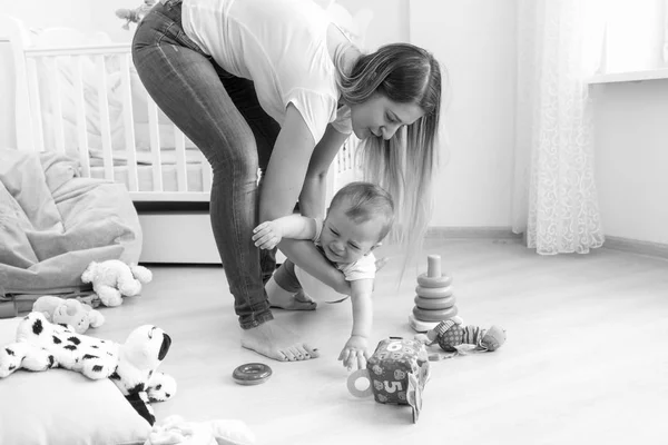 Black and white image of young mother trying to calm down her crying baby boy — Stock Photo, Image