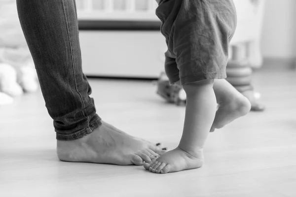 Closeup black and white image of babys feet next to mothers on wooden floor at house — Stock Photo, Image