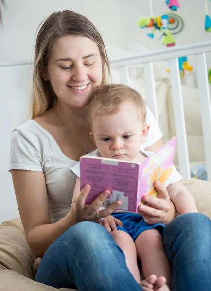 Портрет счастливой улыбающейся молодой женщины, читающей книгу своему 10-месячному сыну — стоковое фото