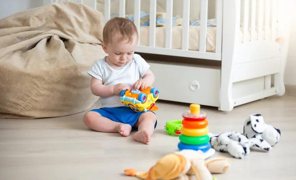 Lindo niño de 10 meses jugando con coche de juguete en el piso en el dormitorio — Foto de Stock