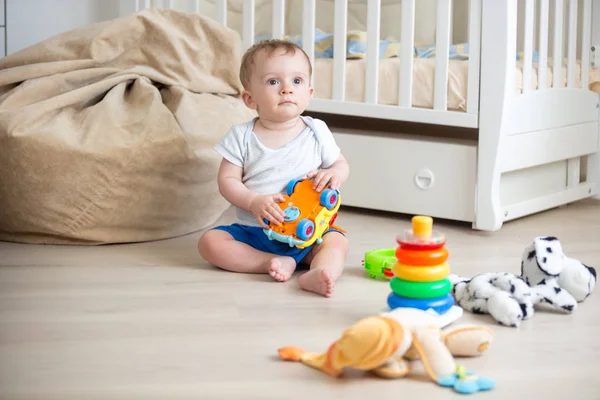 10 meses de idade menino sentado no chão de madeira no quarto e brincando com brinquedos — Fotografia de Stock